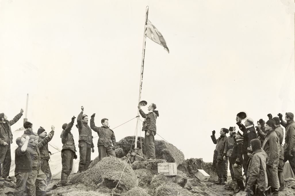 Black and white photo of men standing around a flag