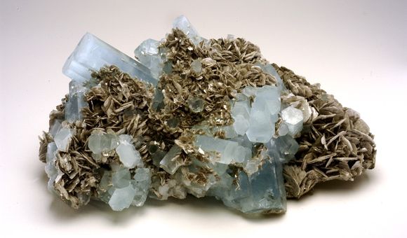 A chuck of natural, light blue and gray aquamarine beryl on white background.
