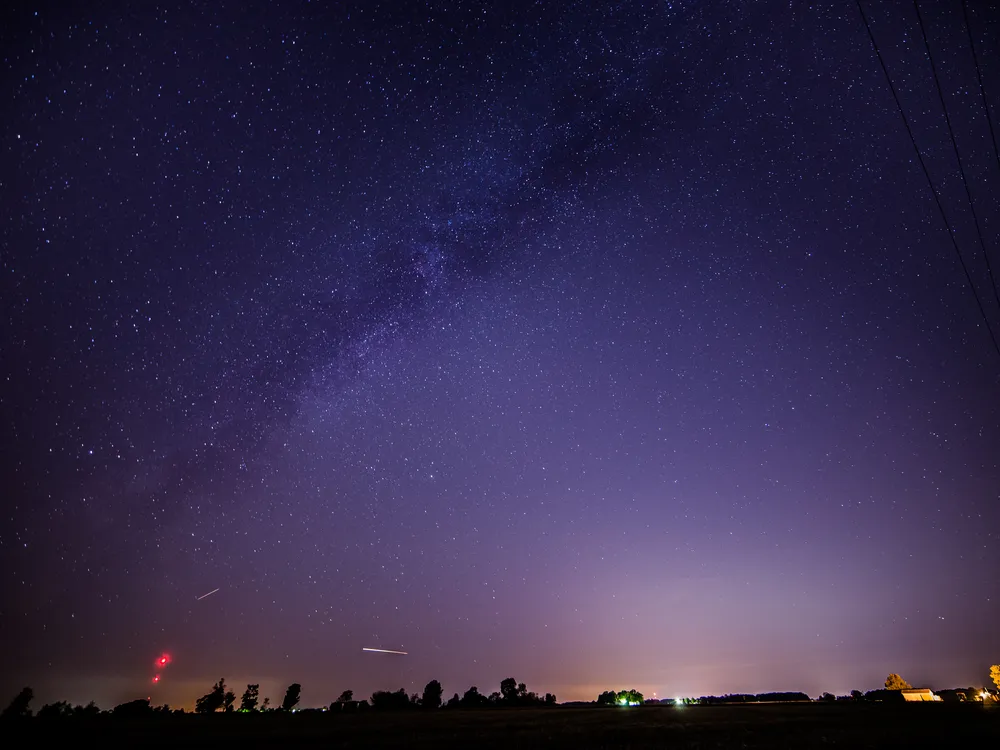 a couple of streaks of light are seen near the horizon in a starry sky that appears purple
