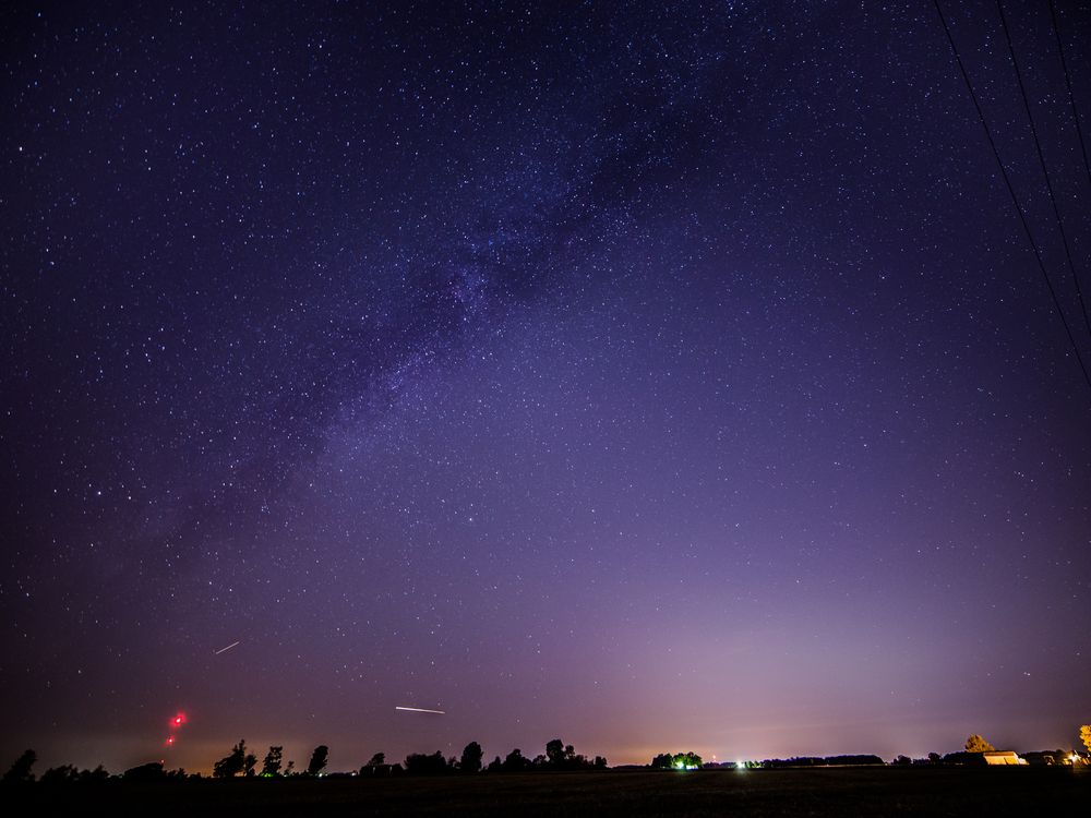 a couple of streaks of light are seen near the horizon in a starry sky that appears purple