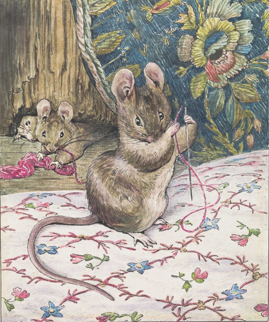 A brown mouse holds a needle and piece of pink thread and works on a delicate embroidery pattern of pink, blue and green flowers on white cloth, while two mice look on behind