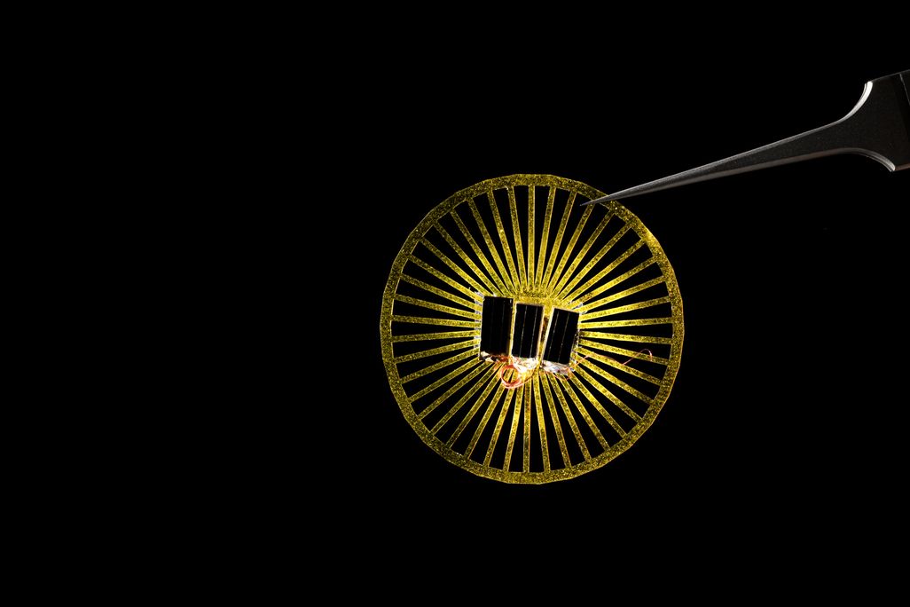 An image of a small wheel like yellow disc with sensors attatched to the middle. A set of tweezers is holding the device against a black background.