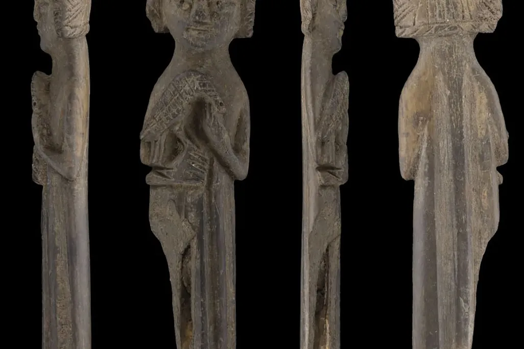 carved wooden figure of person with crown and falcon on right arm
