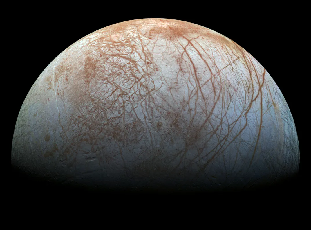 Europa appears white with orange rusty streaks, top half illuminated