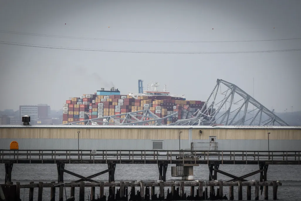 a large container ship in a river with ruins of a truss bridge on top of it
