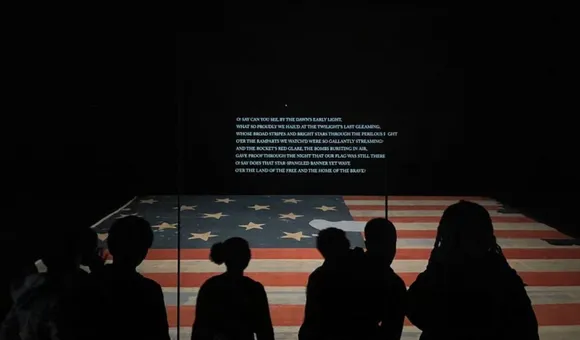 Visitors look at the Star Spangled Banner. It is dimly lit in its gallery at the museum.