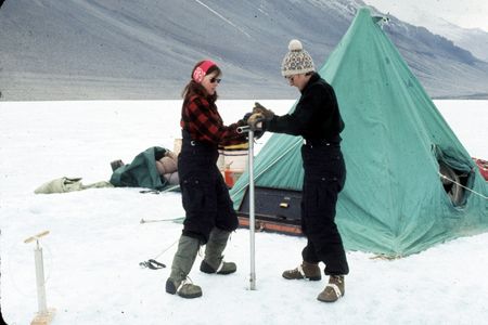 Eileen McSaveney (left) and Terry Tickhill (right) use a hand augur to drill Lake Vanda, Wright Valley, Antarctica, during the 1969-1970 field season. Water collected during this effort was used to date the lake.