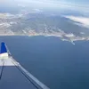 View from a plane’s window showing the wing as the plane flies over the ocean and shoreline.