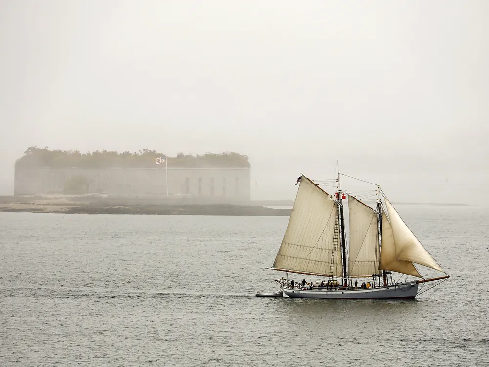 OPENER - Flying Maine’s original state flag, from 1901, the schooner Timberwind sails out of the fog, past Fort Gorges in Casco Bay.