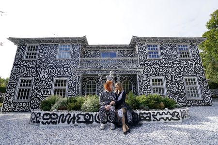 English artist Sam Cox and his wife, Alena, sitting in front of their Kent mansion, which Cox covered in doodles