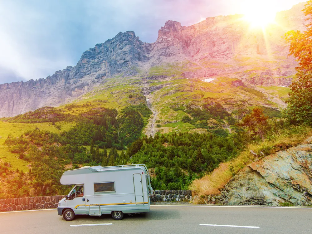 Sun shines brightly on a mountain landscape scene depicting a road with an RV