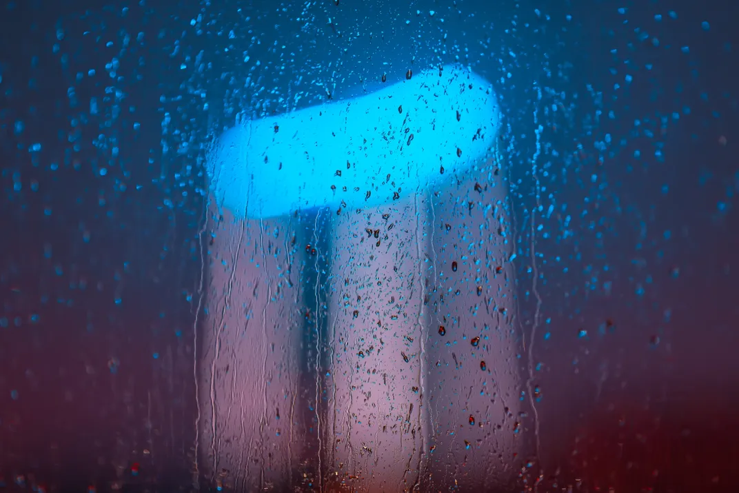 4 - Raindrops pour onto a window during a heavy rainstorm, causing a blurry glow from a high-rise building nearby.