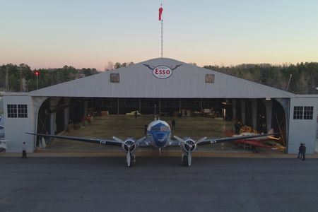 A propellor plane is in front of an open hangar