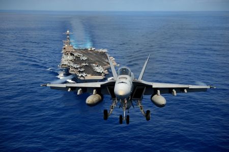 An F/A-18E Super Hornet from the Tophatters of Strike Fighter Squadron (VFA) 14 flies past aircraft carrier USS John C. Stennis in April 2013.
