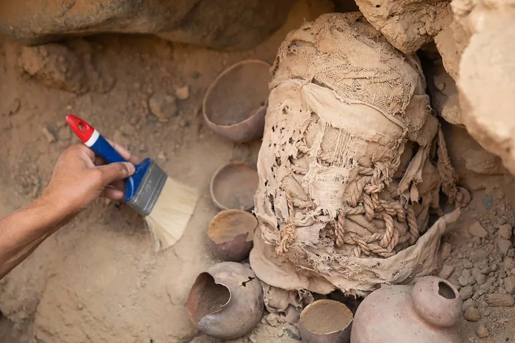 small child's body wrapped in wad of worn cloth being excavated from dirt