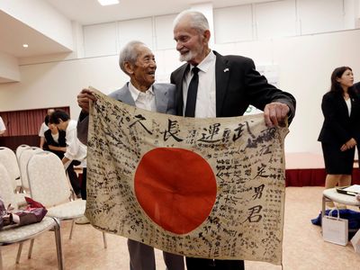 WWII veteran Marvin Strombo, right, and Tatsuya Yasue, an 89-year-old farmer, left, hold a Japanese flag with autographed messages that belonged to Yasue's brother Sadao Yasue, who was killed in the Pacific during World War II.
