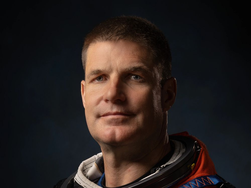 Dramatically-shot portrait of a white male astronaut in an orange spacesuit.
