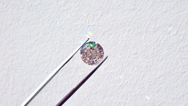Silver tweezers hold a small diamond against a white background.