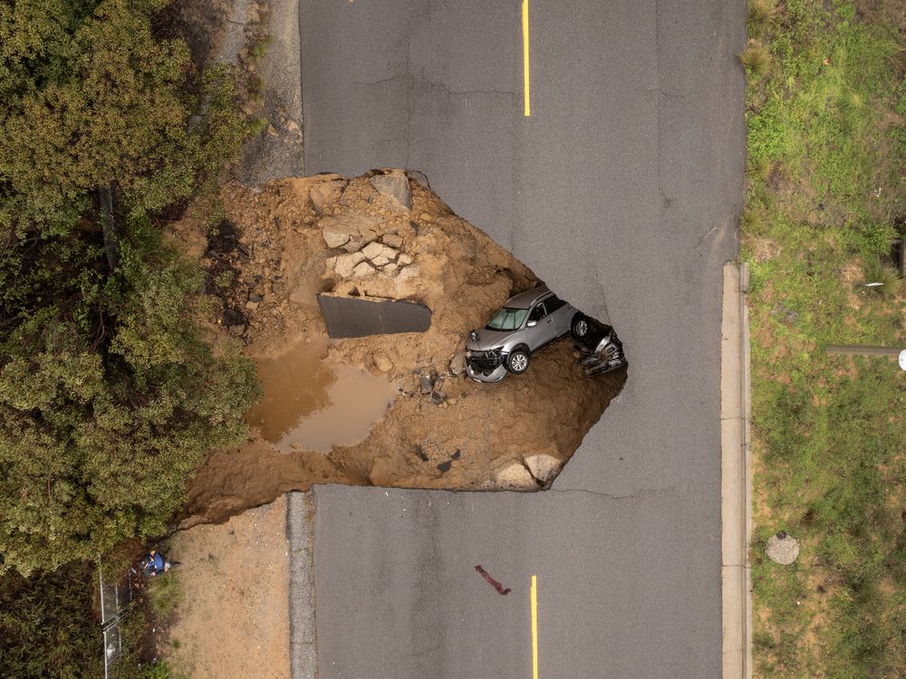 An aerial view of two cars lying in a sinkhole under a road.