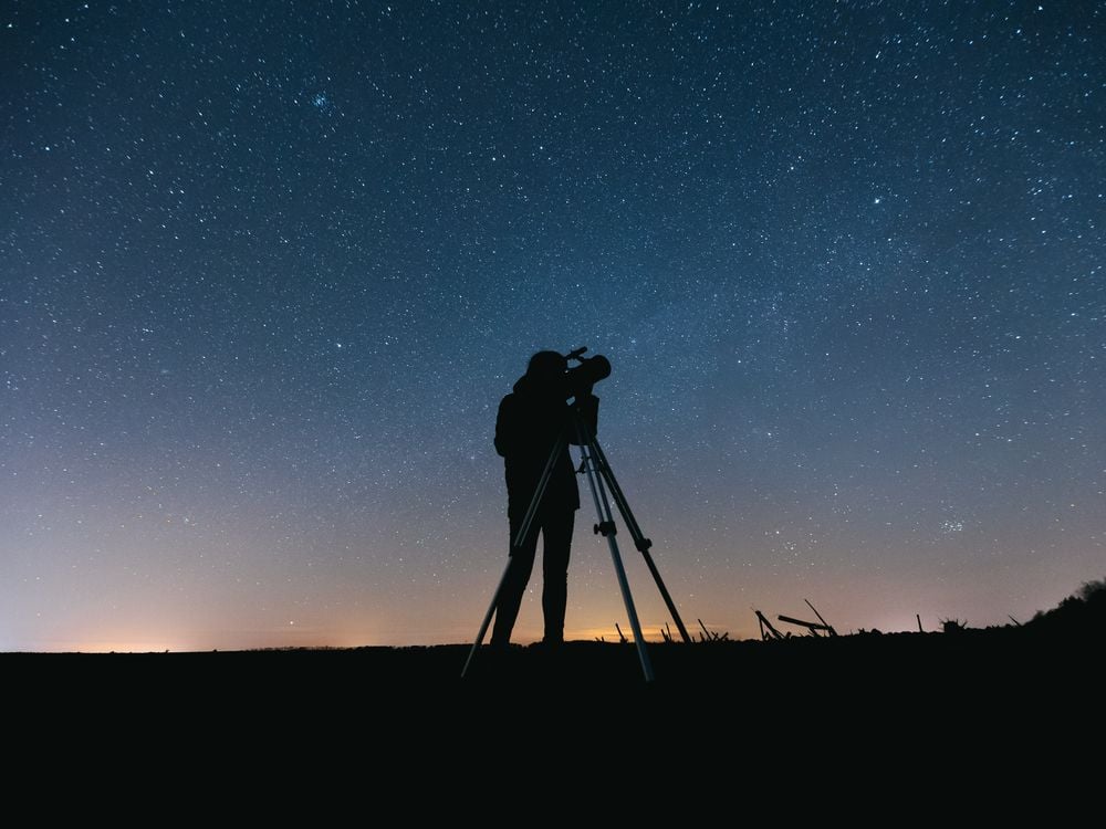 a person with a telescope in front of a starry sky