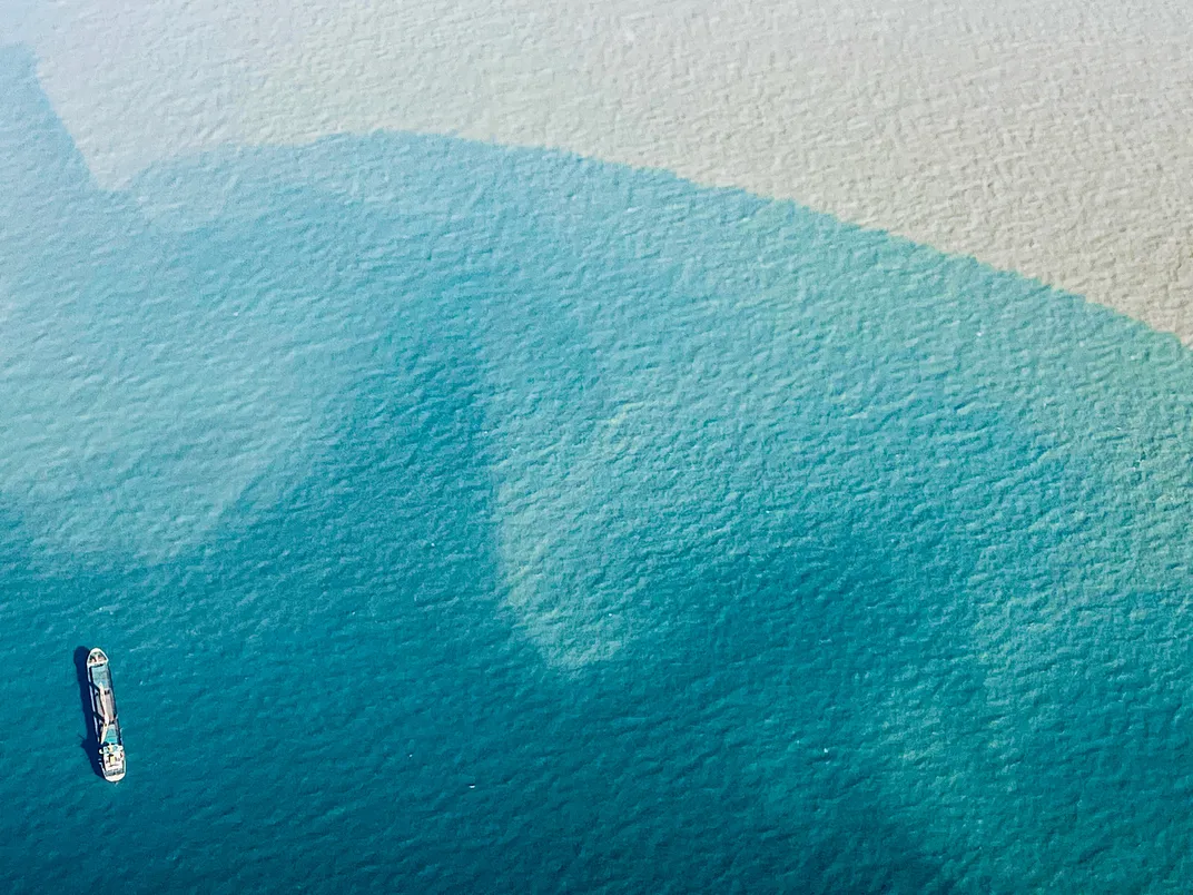 A cargo ship moves slowly on rippling, peaceful waters reflecting different shades of blue.