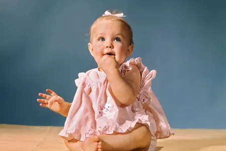A 1960s studio portrait of a baby girl wearing a pink dress