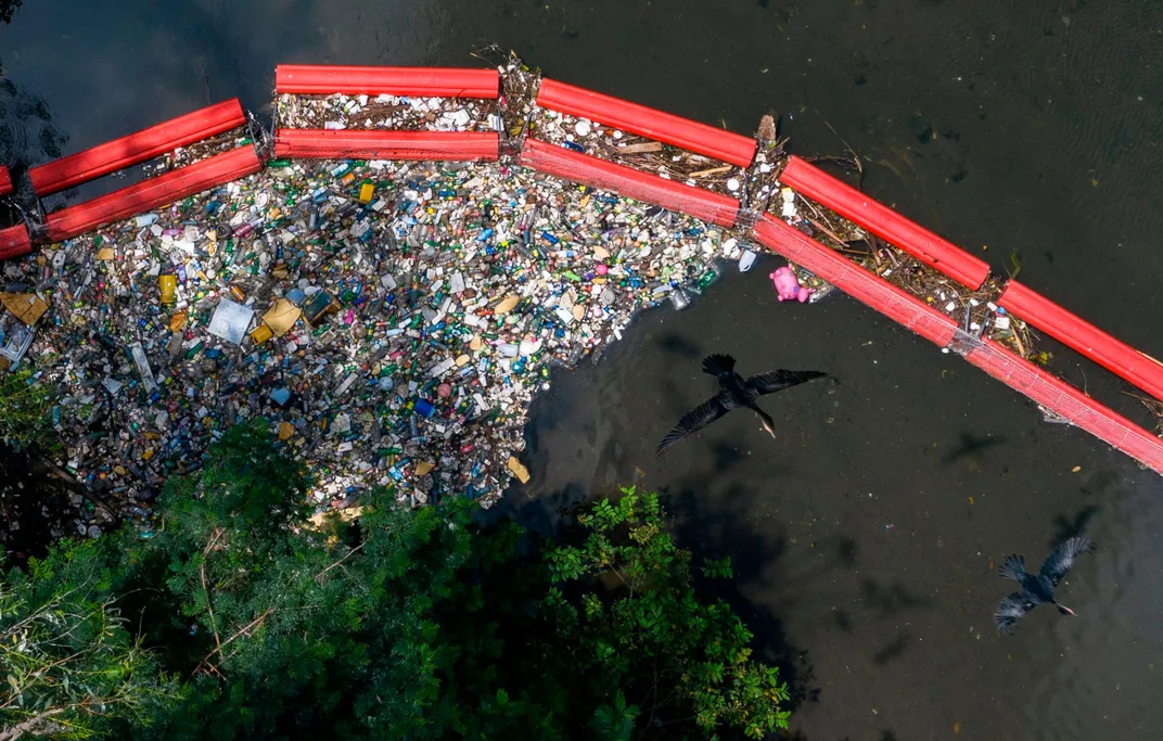 Aerial view of plastic corralled by a floating booming as two birds fly over