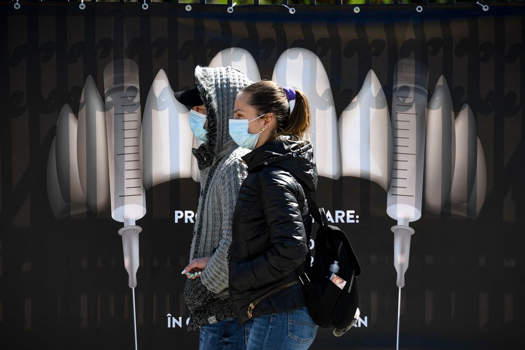 People wearing protection masks walk by a banner showing syringes as vampire fangs during the vaccination marathon organized at the "Bran Castle" in Bran village on May 8, 2021