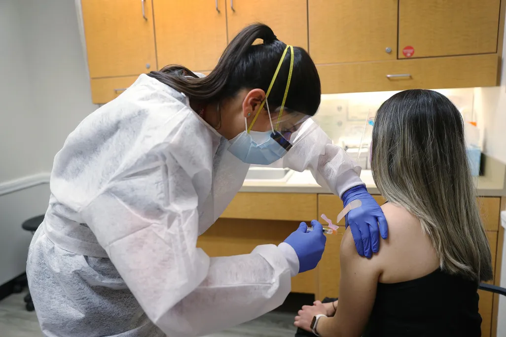 A nurse practitioner wears personal protection equipment as she administers a flu vaccination to a patient