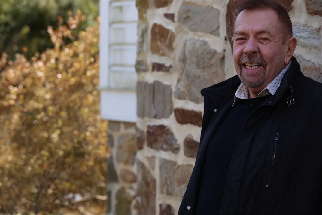 a man smiles and stands against a stone building