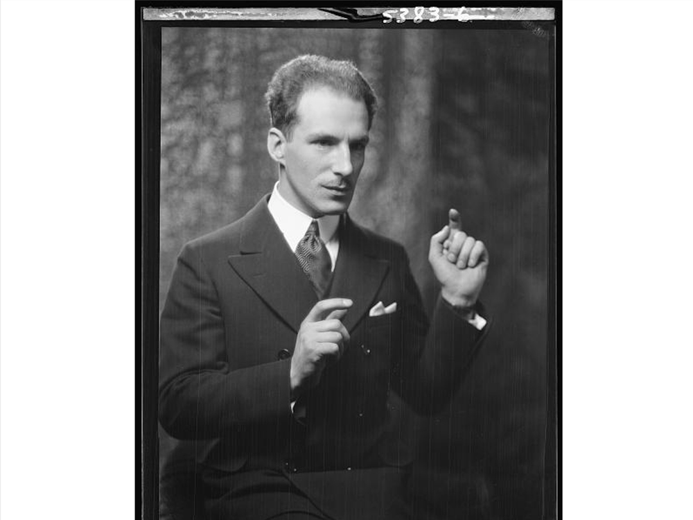 A black and white photograph of Theremin from the waist up, holding one hand up and his other to the side as though he is playing his namesake instrument