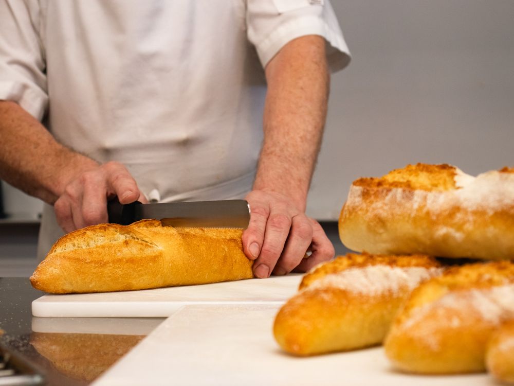 Chef cutting a loaf of bread with other loaves nearby
