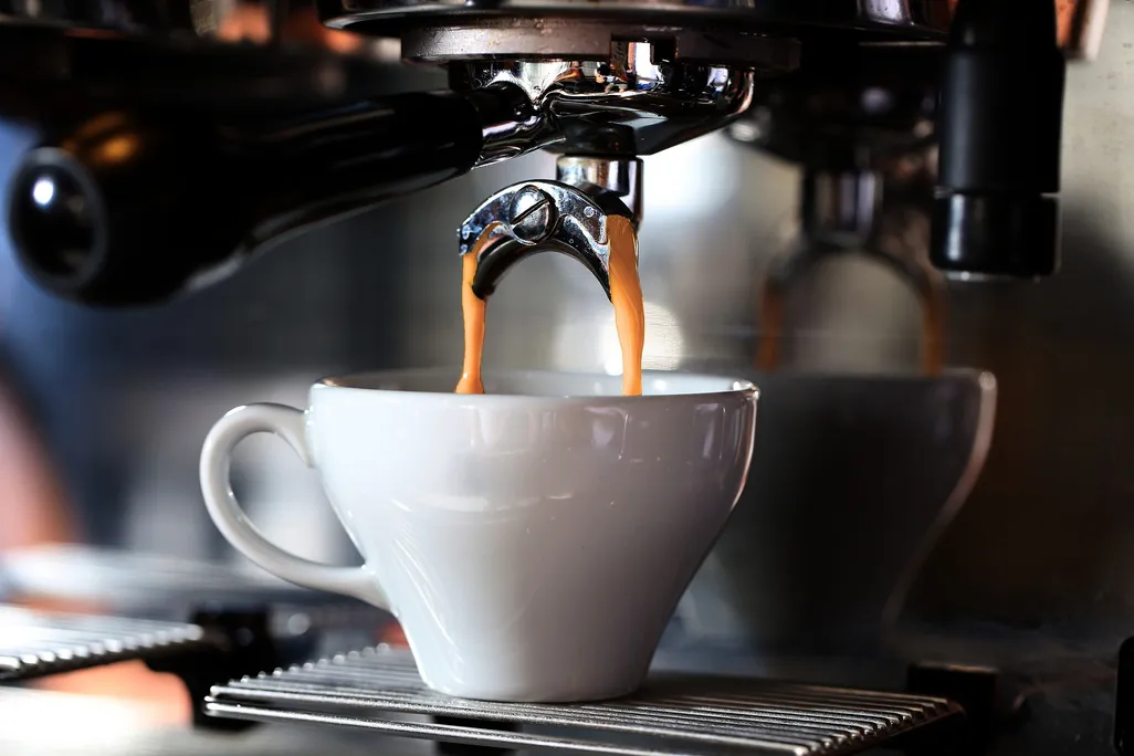 Coffee pouring into small white cup from espresso maker