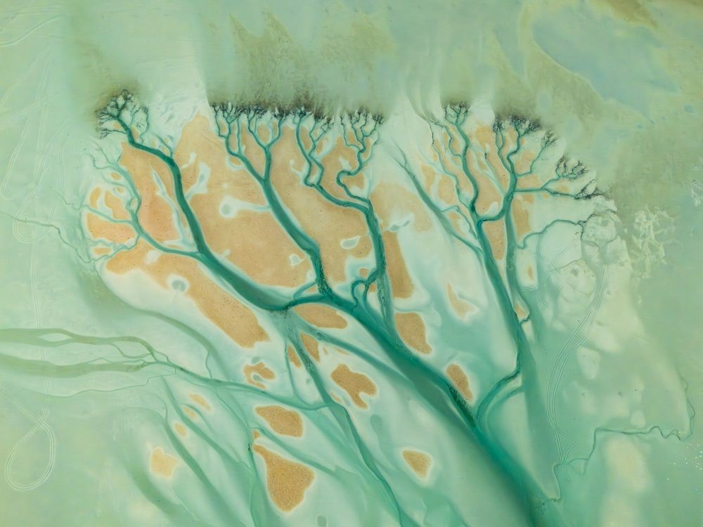 Captured from above in Qassabi, Abu Dhabi, this photograph reveals a delicate dialogue between sea and sand. Turquoise tidal channels branch organically across the shallow waters, resembling the veins of a living landscape. Patches of exposed sand emerge within the sea itself, blurring the boundary between land and water. From this aerial perspective, nature transforms into abstraction—where flowing currents carve their own patterns, and the coastline becomes a quiet canvas shaped by time, movement, and tide.