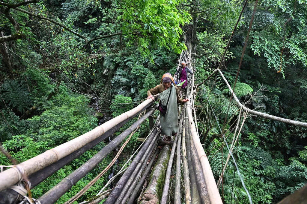 Khasi tribal women walk across a root bridge in Mawkyrnot village