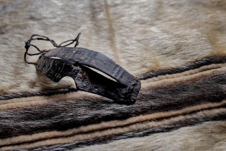 Inupiaq goggles carved from baleen set against a Tunumiit (East Greenland Eskimo) woman’s sealskin parka. Both are from the collection of the National Museum of the American Indian.