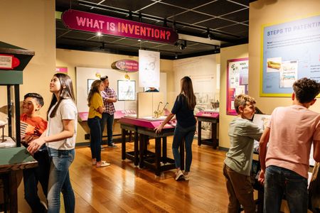 Seven people- adults and children- interact with the Nation of Inventors exhibition gallery