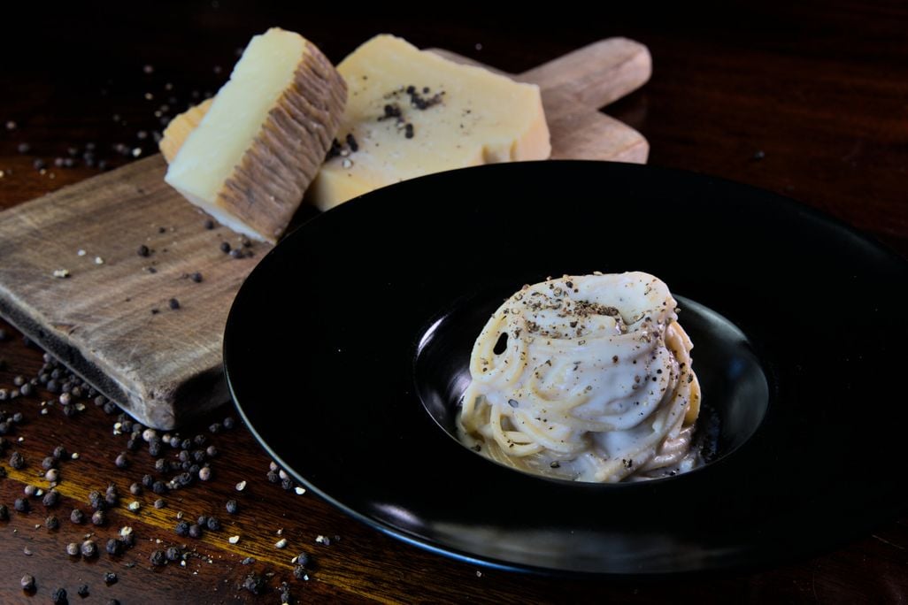 a plate of cacio e pepe in front of a cheeseboard.