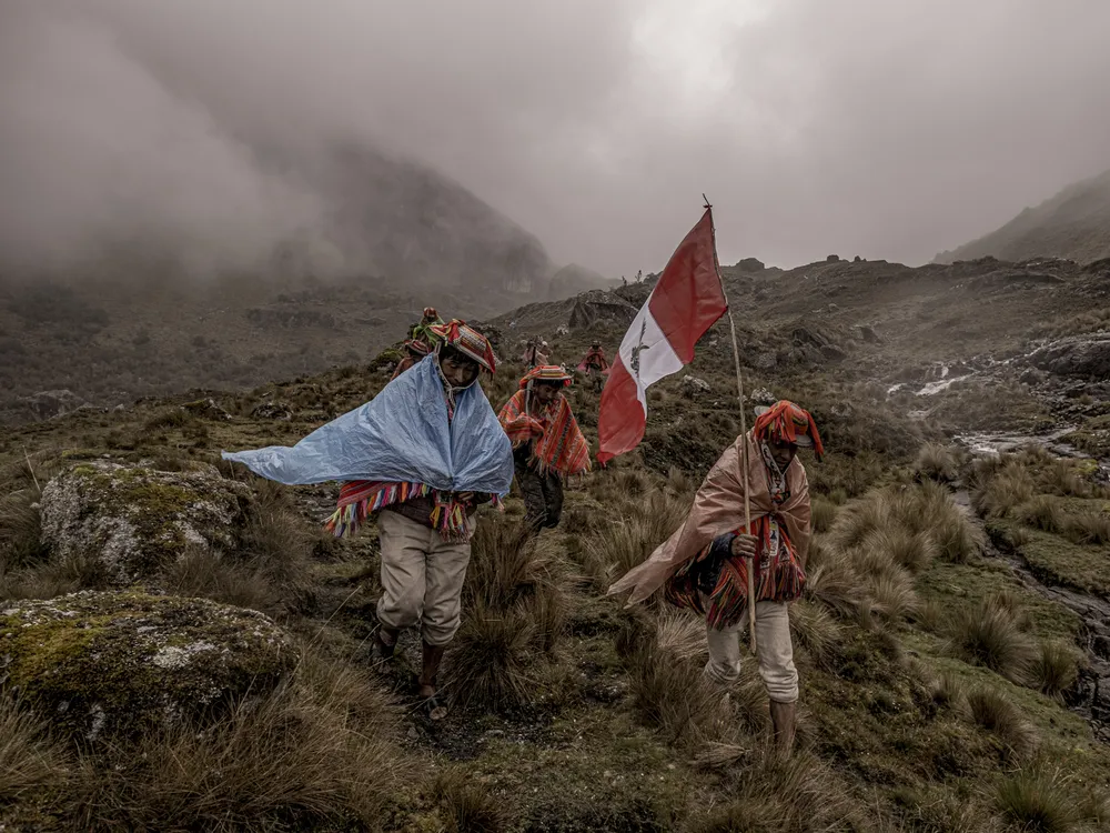 people walk in fog through mountains carrying the Peruvian flag and wrapped in cloths