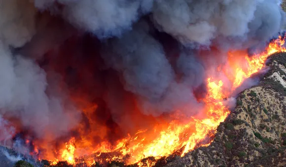 Gray smoke billows from fires on a mountainside, as seen from above.
