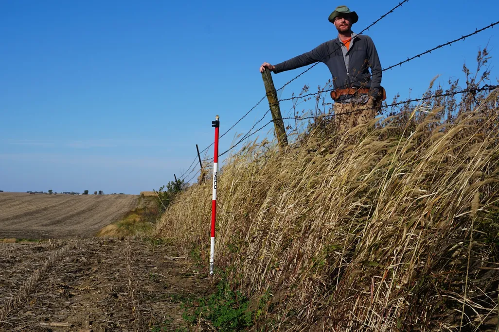An image of a reseacher standing on native prairie a few feet above degraded farmed land.