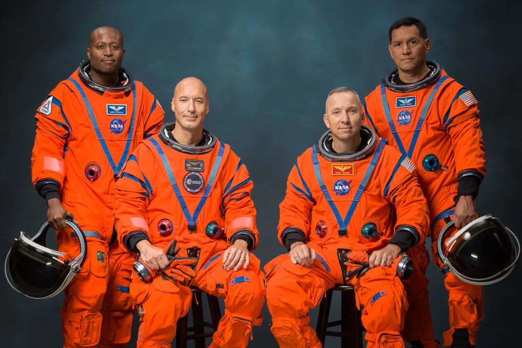 four men in orange spacesuits pose for a picture