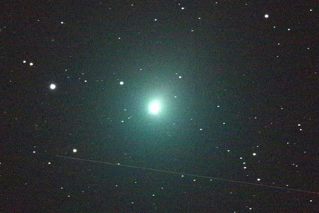 A photo of Comet 46P/Wirtanen. In the middle of the image is a ball of light that is glowing bright green against a starry black sky. 
