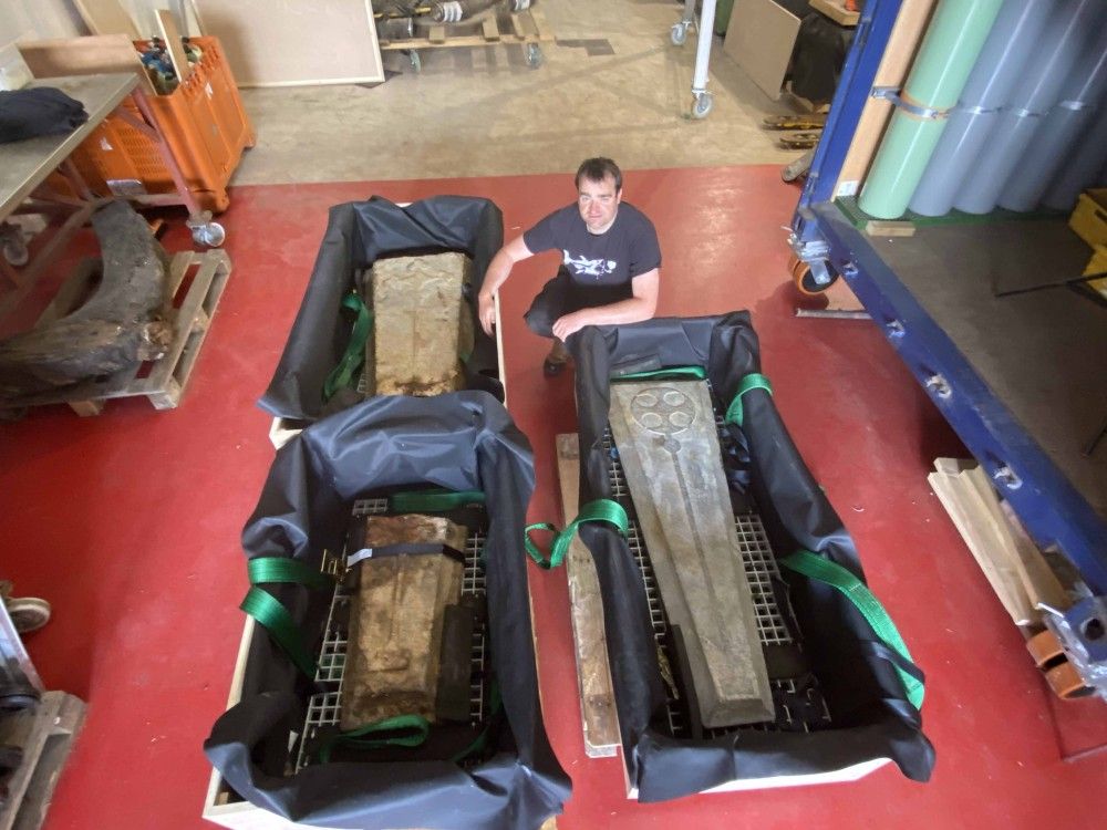 Man squatting down next to open-topped crates with grave slabs in them
