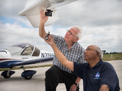 Rafat Ansari of NASA Glenn (right) helps attach a camera to a volunteer pilot's aircraft.