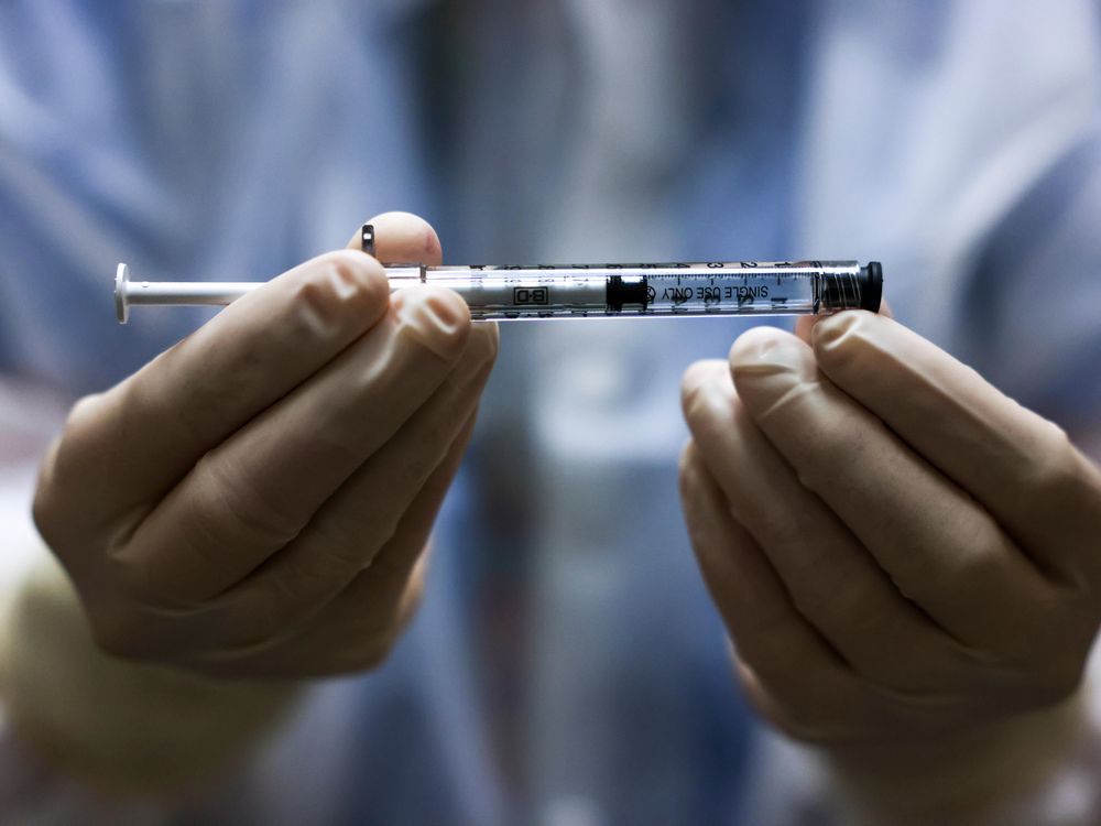 A pharmacy technician's gloved hands hold a dose of the Johnson & Johnson Covid-19 vaccine 