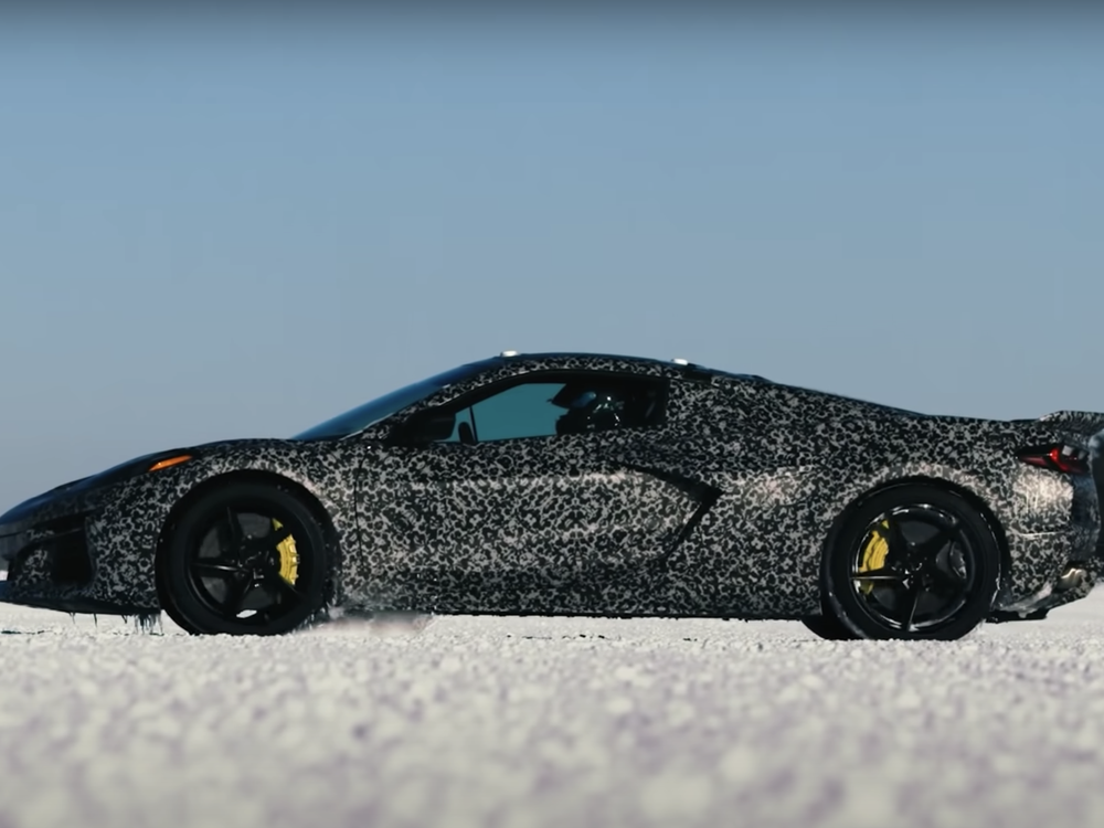 An image of a Corvette with a camouflage wrap sitting idle in snow. The car also has yellow calipers by near its black rimmed wheels.