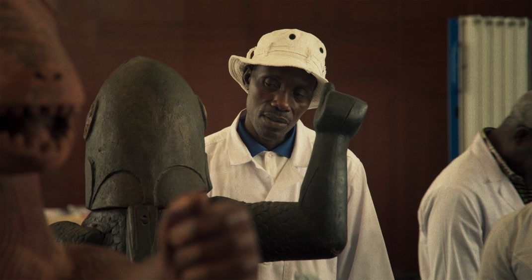 A man looks at a wooden statue. He wears a white hat.