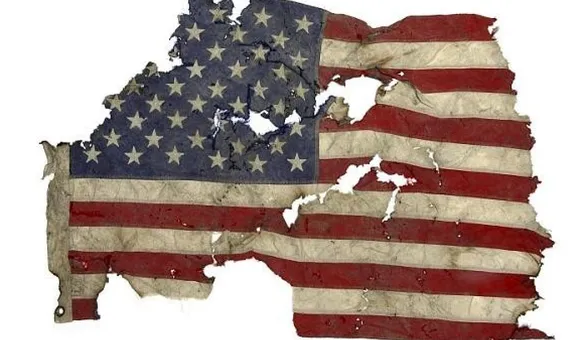 A tattered, torn, and singed American flag displayed against a white background.