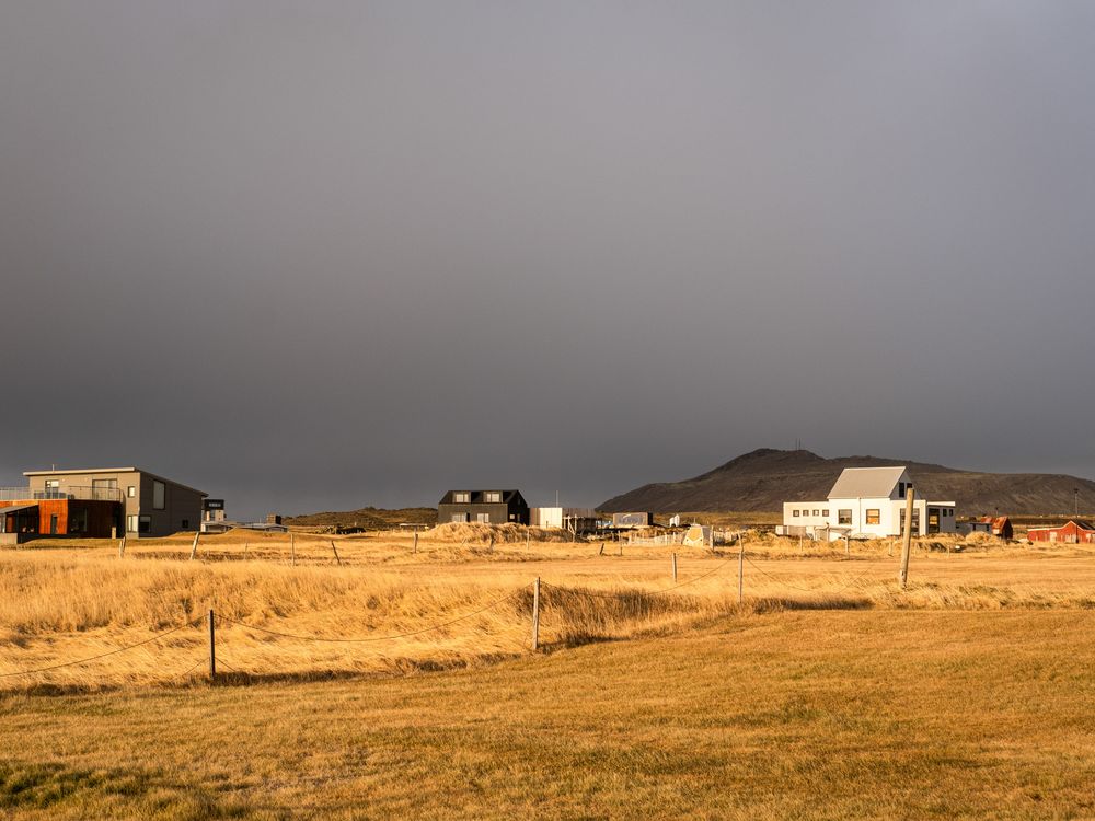 A couple of buildings at the back of a field with a dark sky overhead